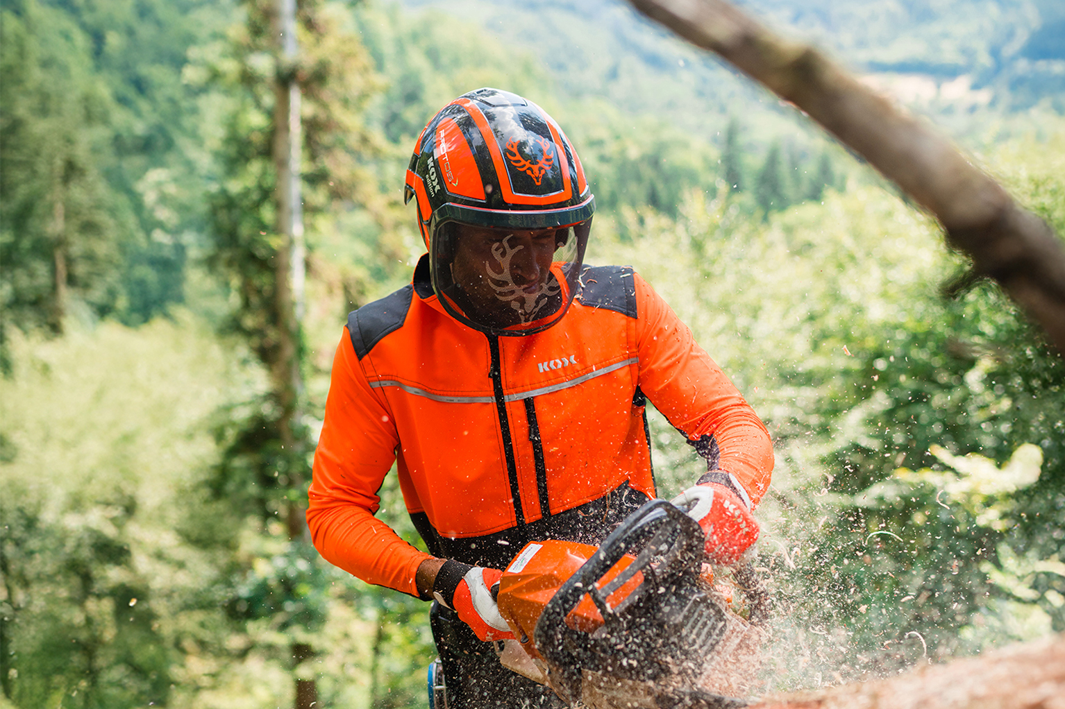 Un ouvrier forestier en tenue de protection orange d�coupe un tronc d’arbre couch� avec une tron�onneuse.