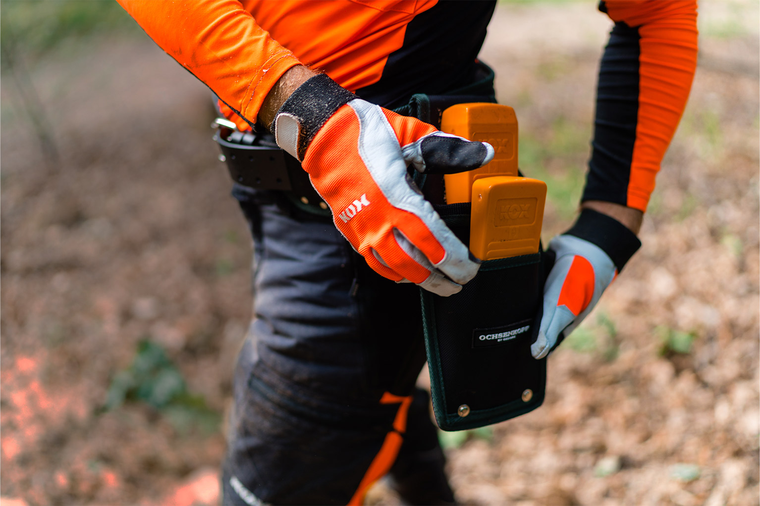 Une personne en tenue de protection orange range des coins KOX orange dans une sacoche � outils � la ceinture.